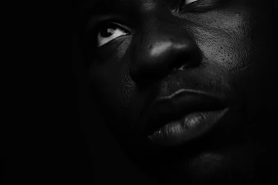 A close-up portrait of a person with dramatic lighting and deep shadows on a black background.