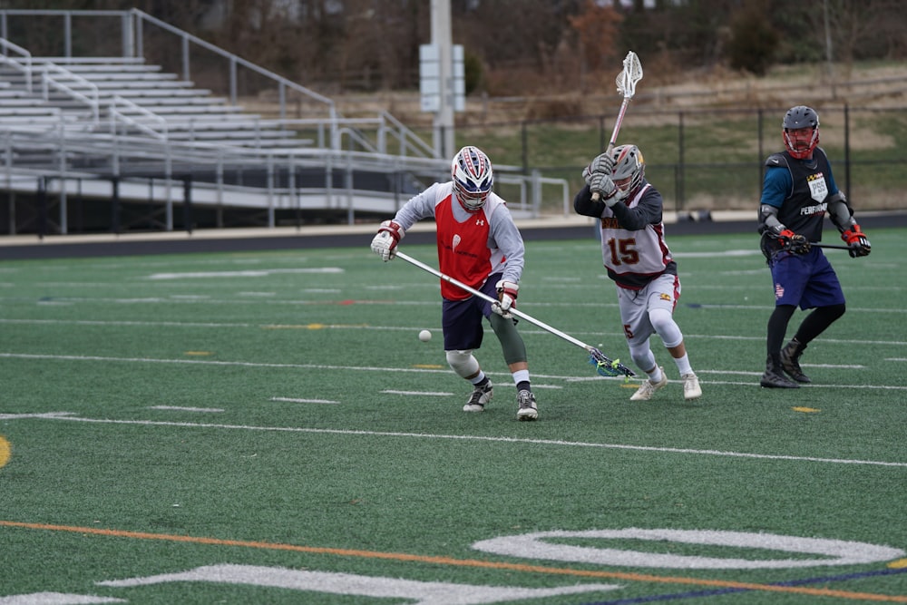 three person playing lacrosse on field during daytime