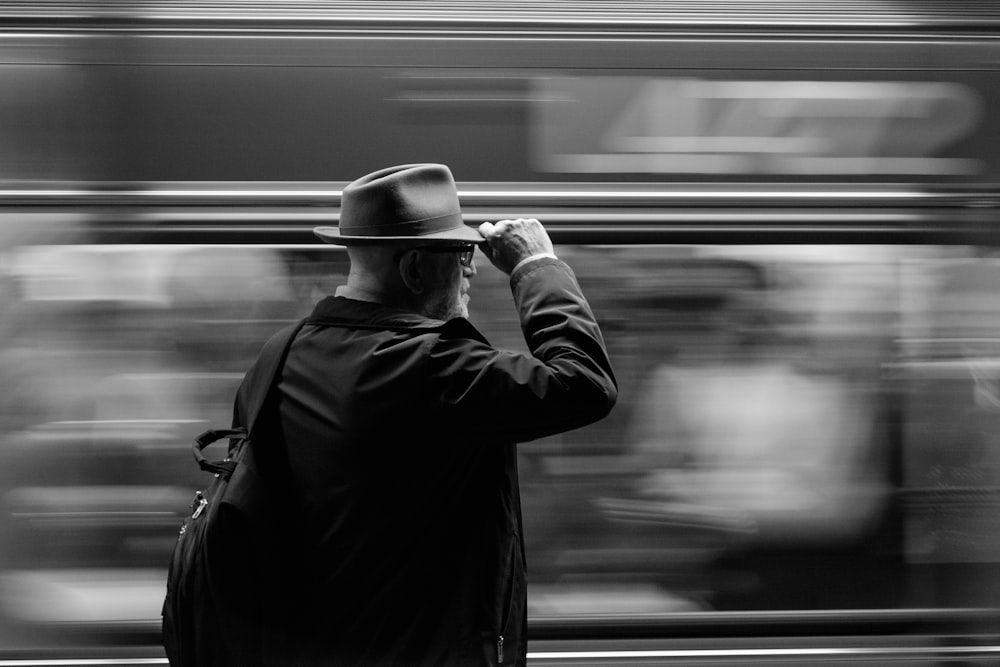 grayscale photography of man holding his hat