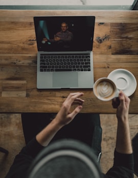 person holding cup of latte while facing MacBook Pro