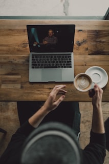 person holding cup of latte while facing MacBook Pro