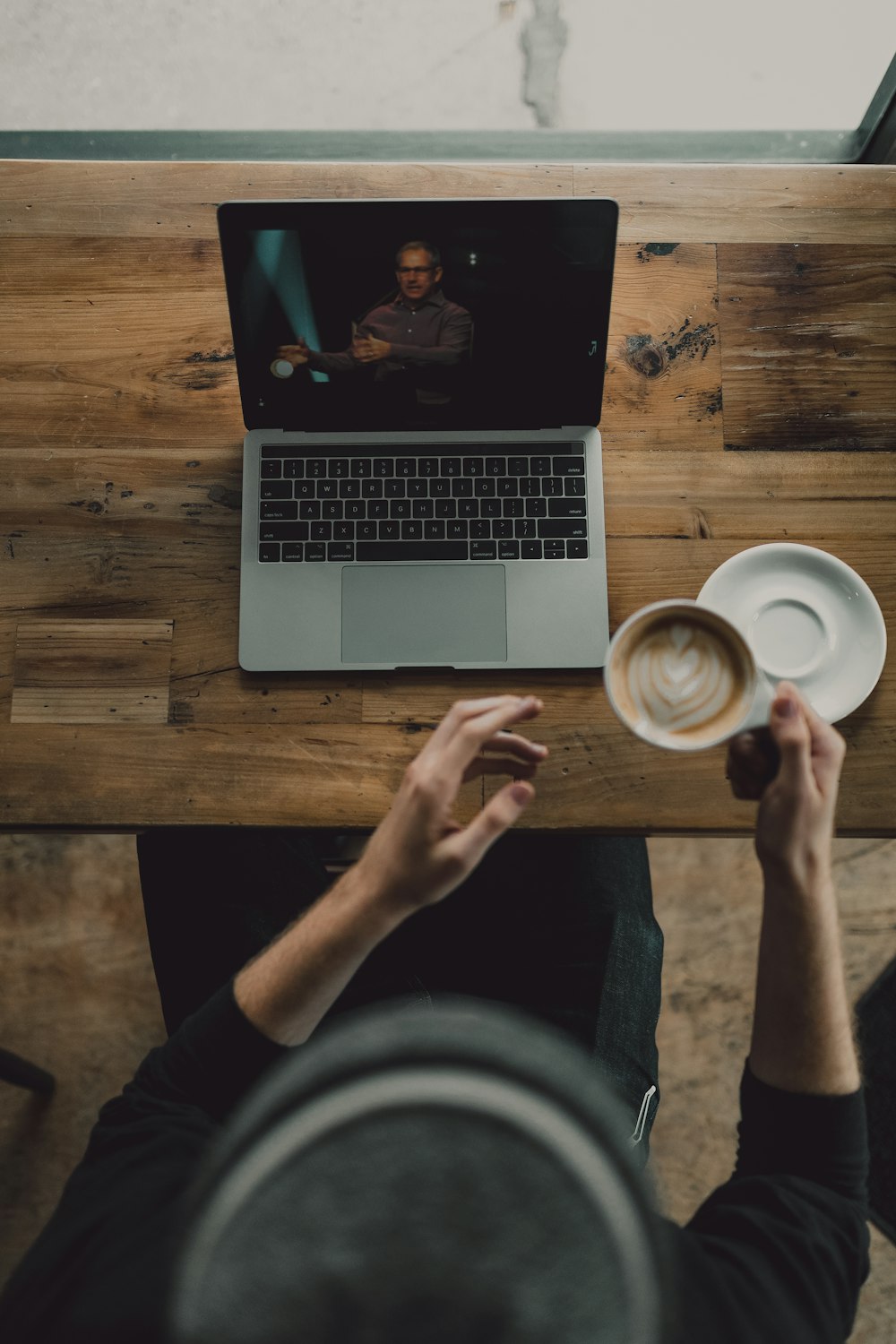 persona sosteniendo una taza de café con leche mientras mira a la MacBook Pro