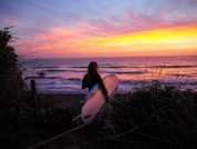 woman holding surfboard front of the sea during golden hour