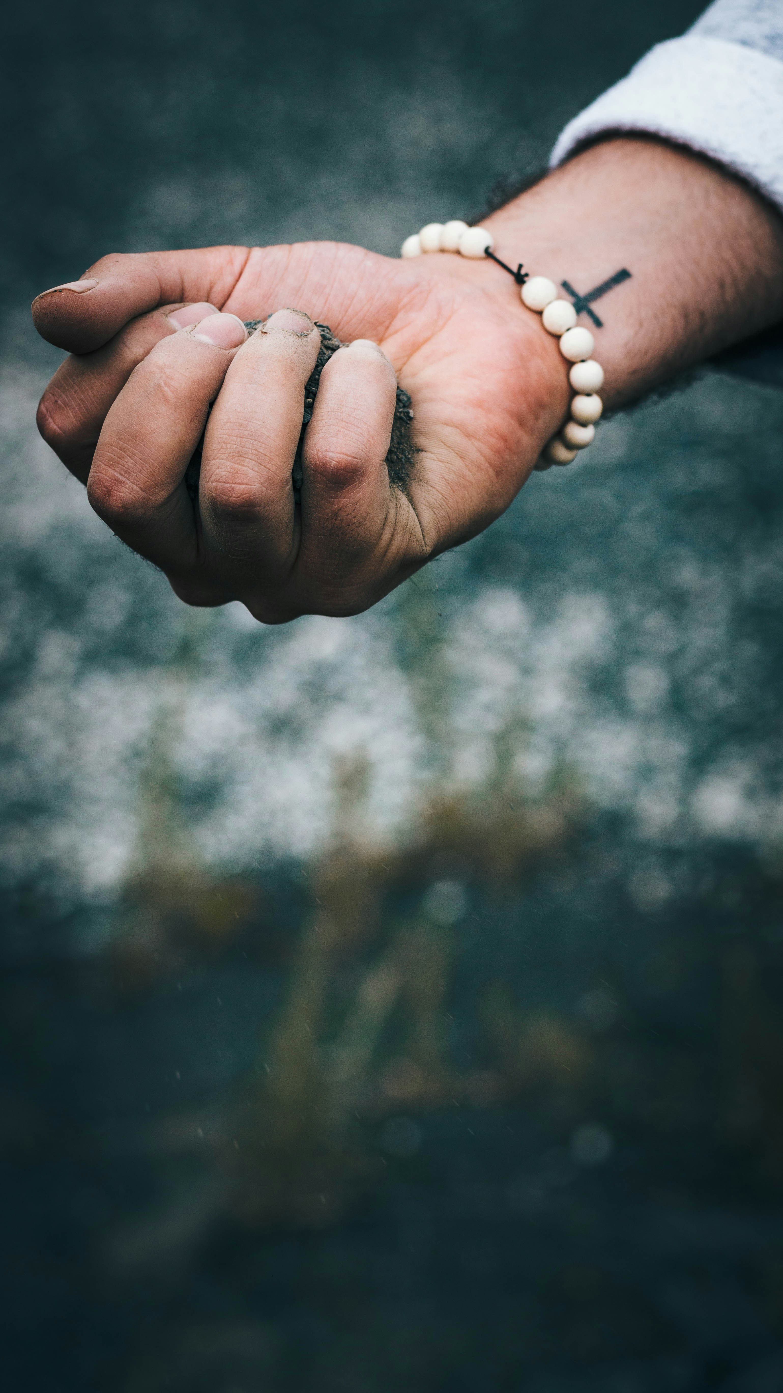 person wearing beaded white bracelet with dirt in hand