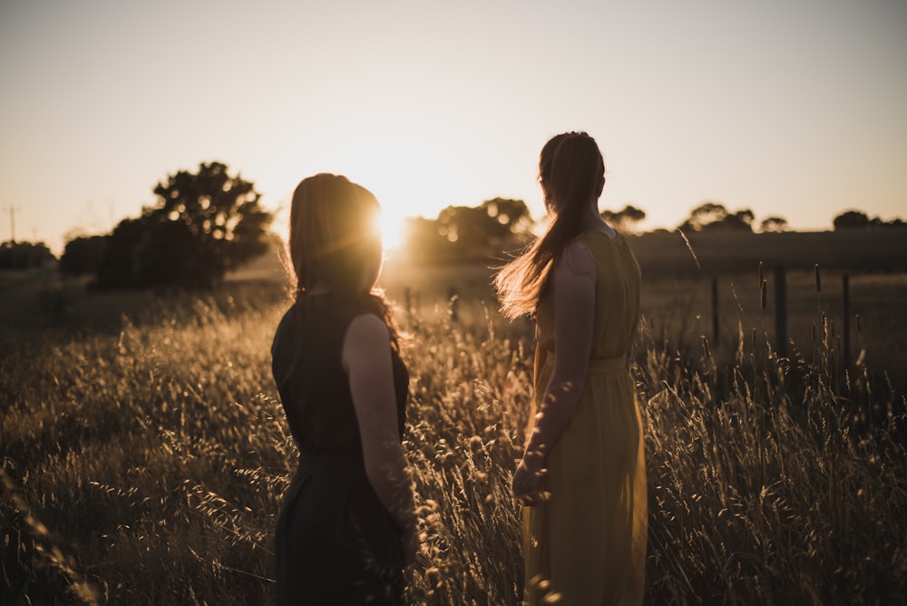 two women standing on grass field during golden hour