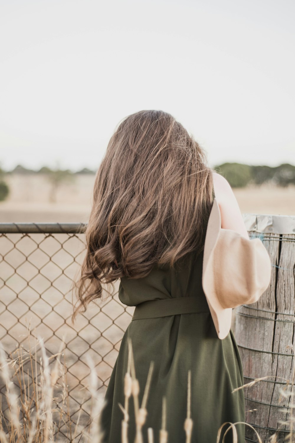 woman wearing green sleeveless dress standing next to chain-link fence during daytime