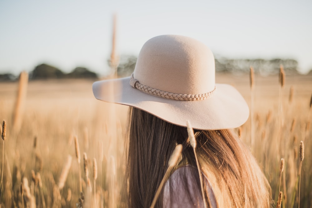 Frau mit beigefarbenem Sonnenhut steht auf Weizenfeld