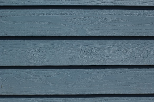 A close-up view of horizontal wooden planks painted in a muted blue color, featuring subtle wood grain textures and lines.