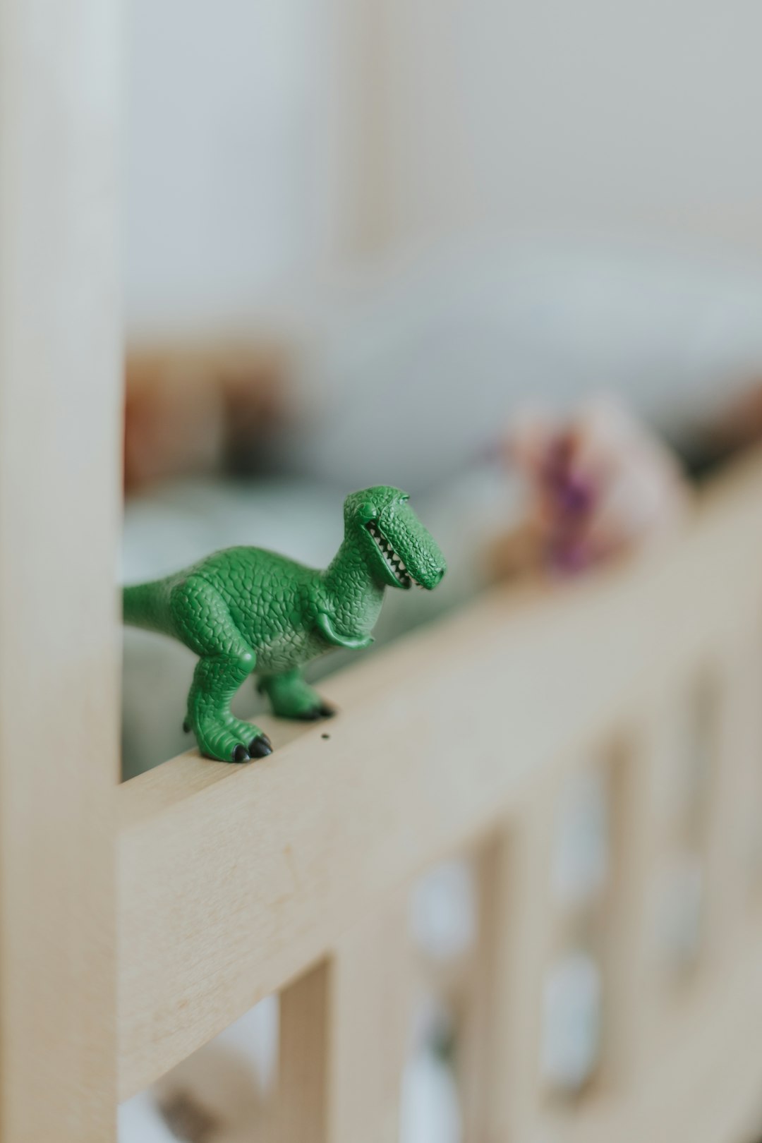 selective focus photography of green dinosaur scale model on brown wooden crib