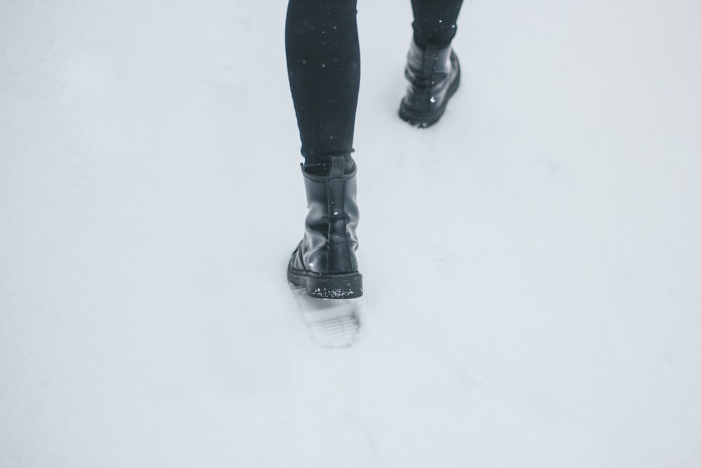 person wearing black leather boots stepping on snow