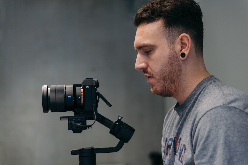 man wearing gray crew-neck shirt looking at black digital camera with camera stabilizer