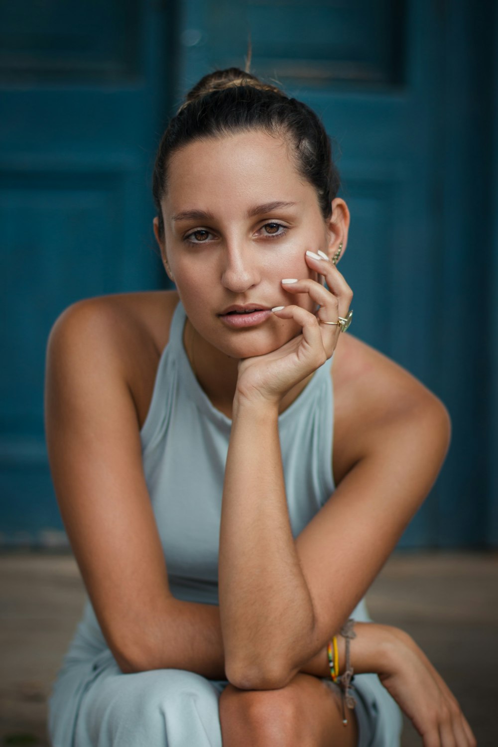 shallow focus photo of woman in gray sleeveless dress sitting near blue door