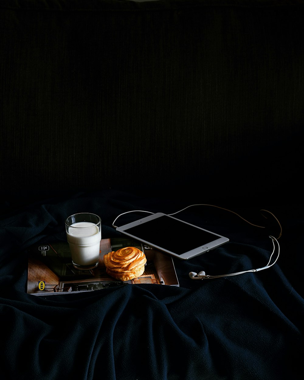 silver iPad beside clear drinking glass on black textile