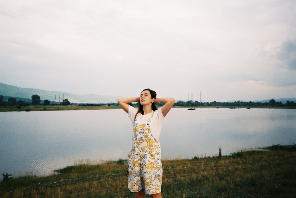 woman in floral dungaree holding hair while standing near lake