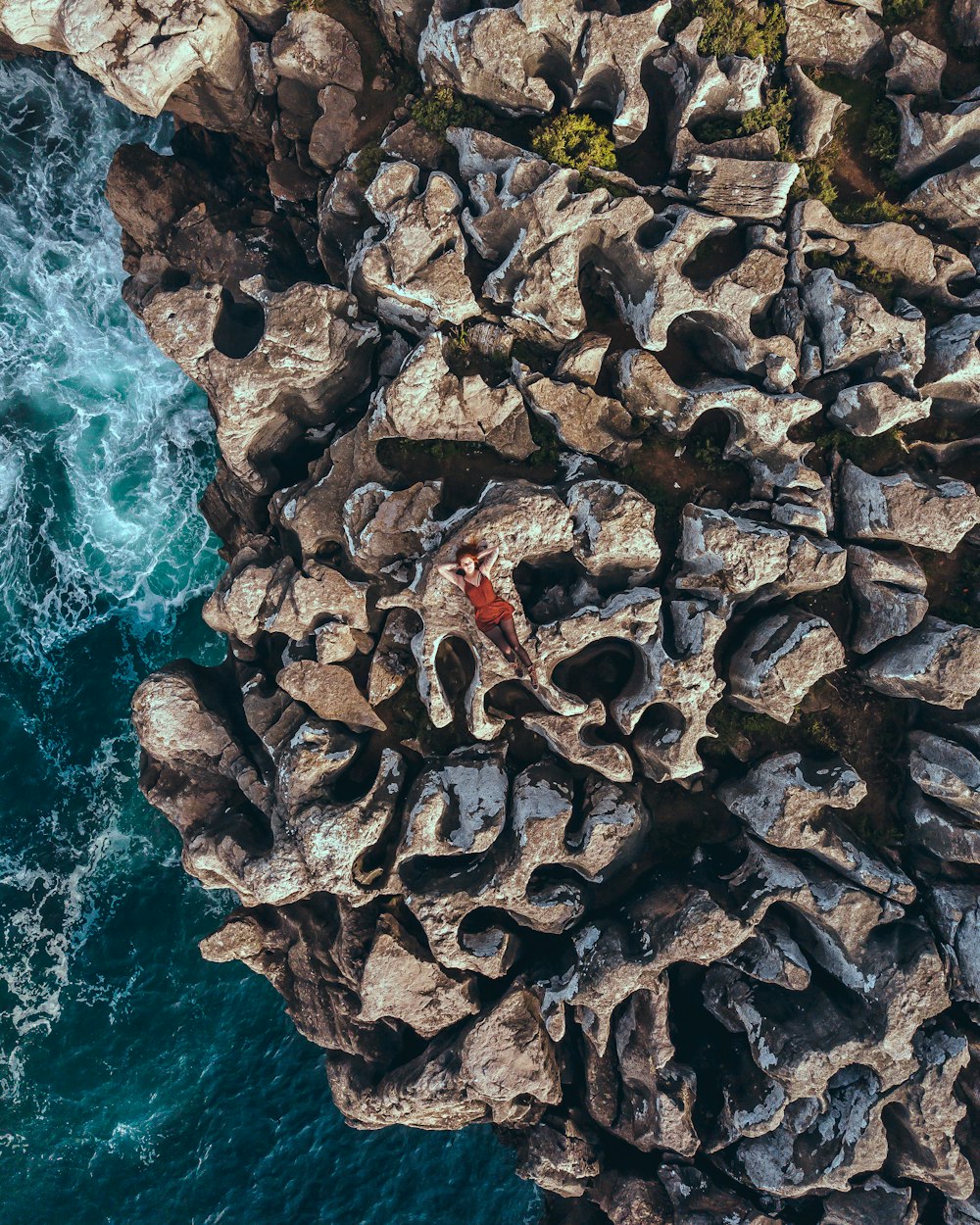 woman in red tank top lying on grey stone formation near sea