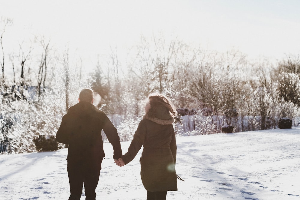 couple holding hand while walking on snow covered field
