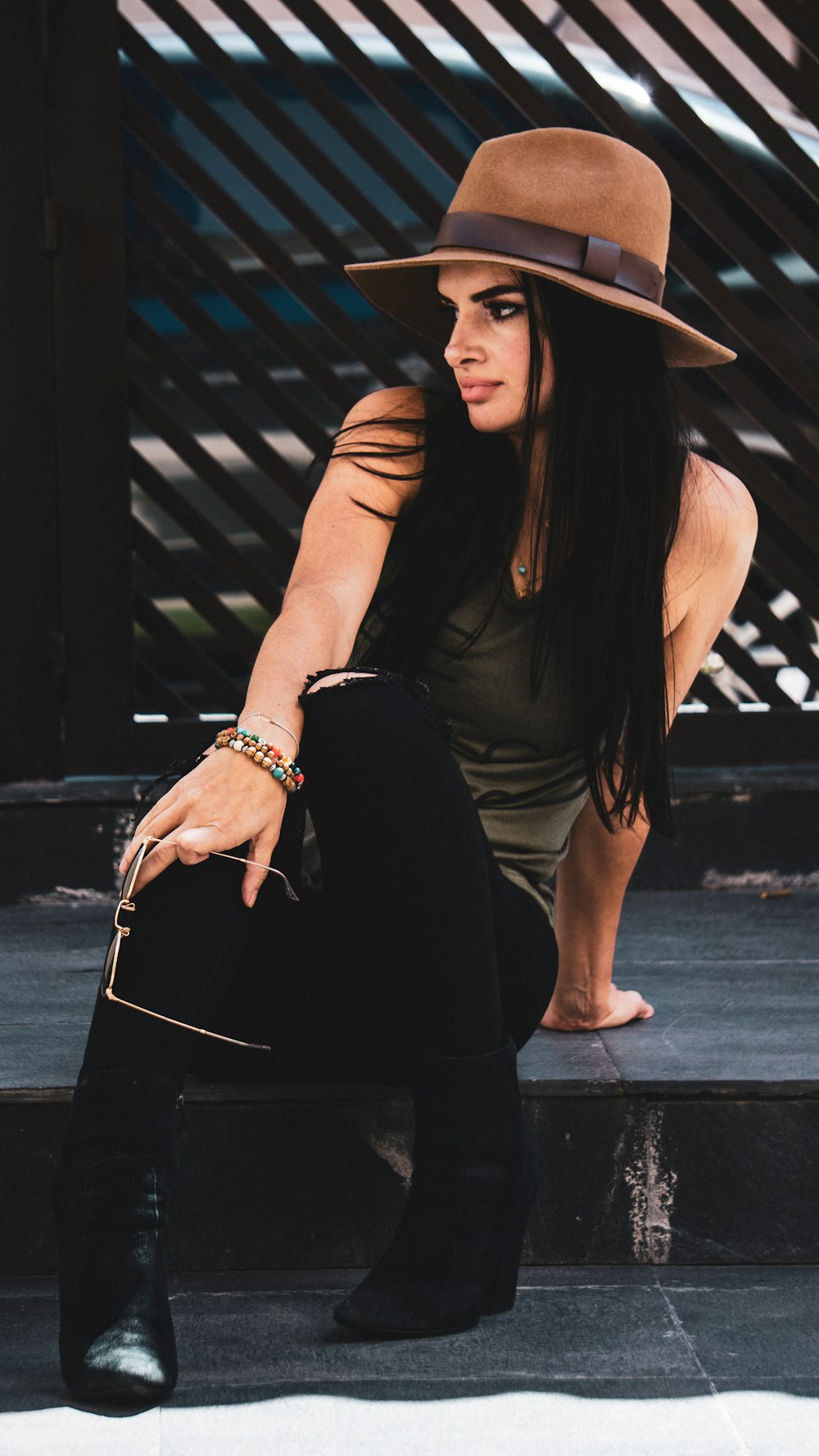 woman wearing brown fedora hat, brown tank top and black pants sitting on concrete floor