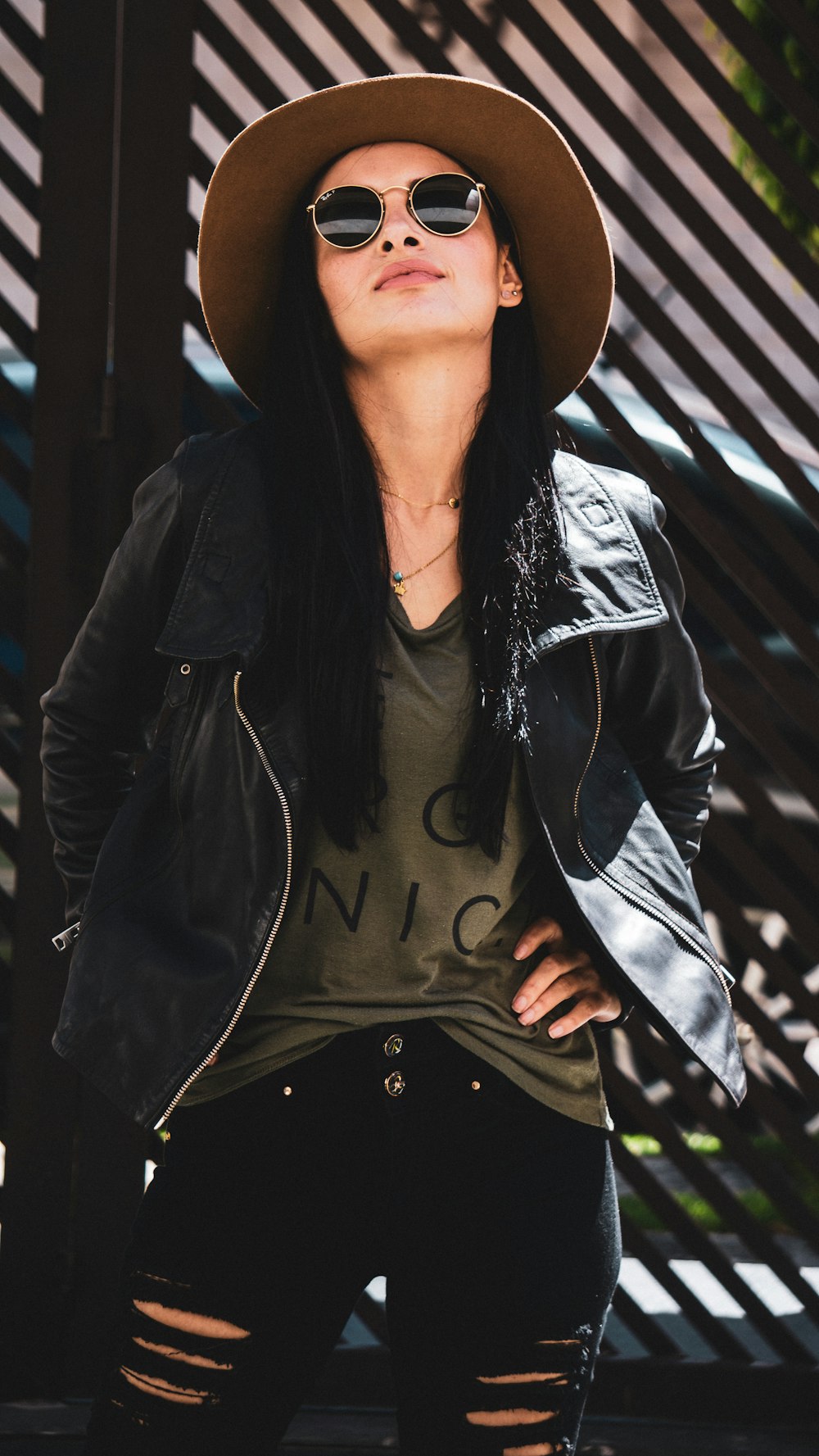 woman wearing hat and jacket leaning on black wall