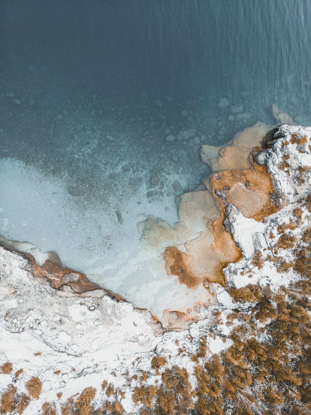 Fotografía aérea de un acantilado cubierto de nieve cerca de un cuerpo de agua durante el día