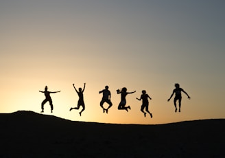 six silhouette of people jumping during sunrise