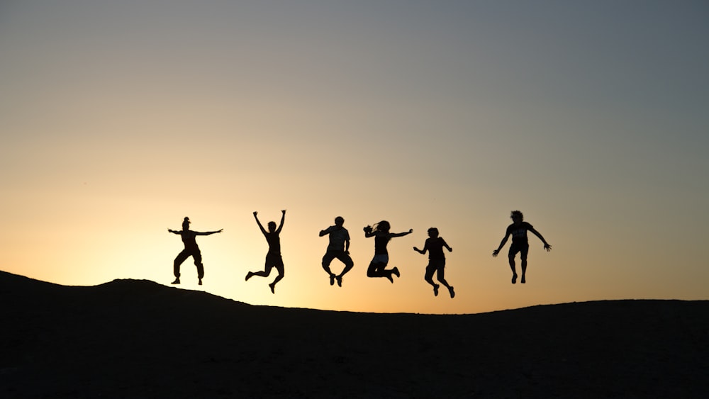 Seis siluetas de personas saltando durante la salida del sol
