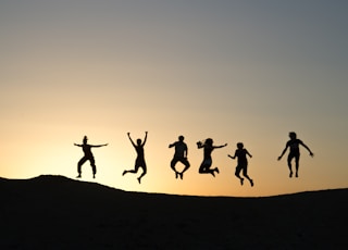 six silhouette of people jumping during sunrise