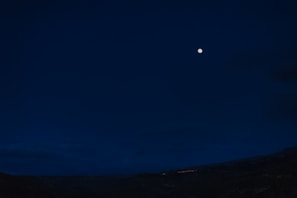 A serene night sky with a bright full moon illuminating a landscape.