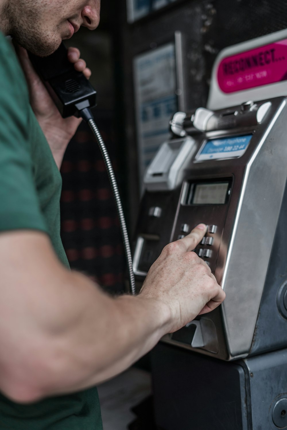 man in green shirt dialing on public phone