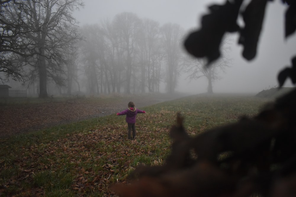 child standing on green grass with leaves during daytime