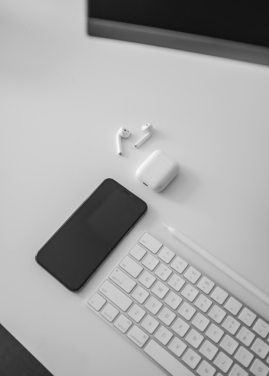 black iPhone X, Air pods, and Apple keyboard on desk