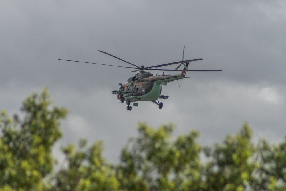 green helicopter flying under cloudy sky