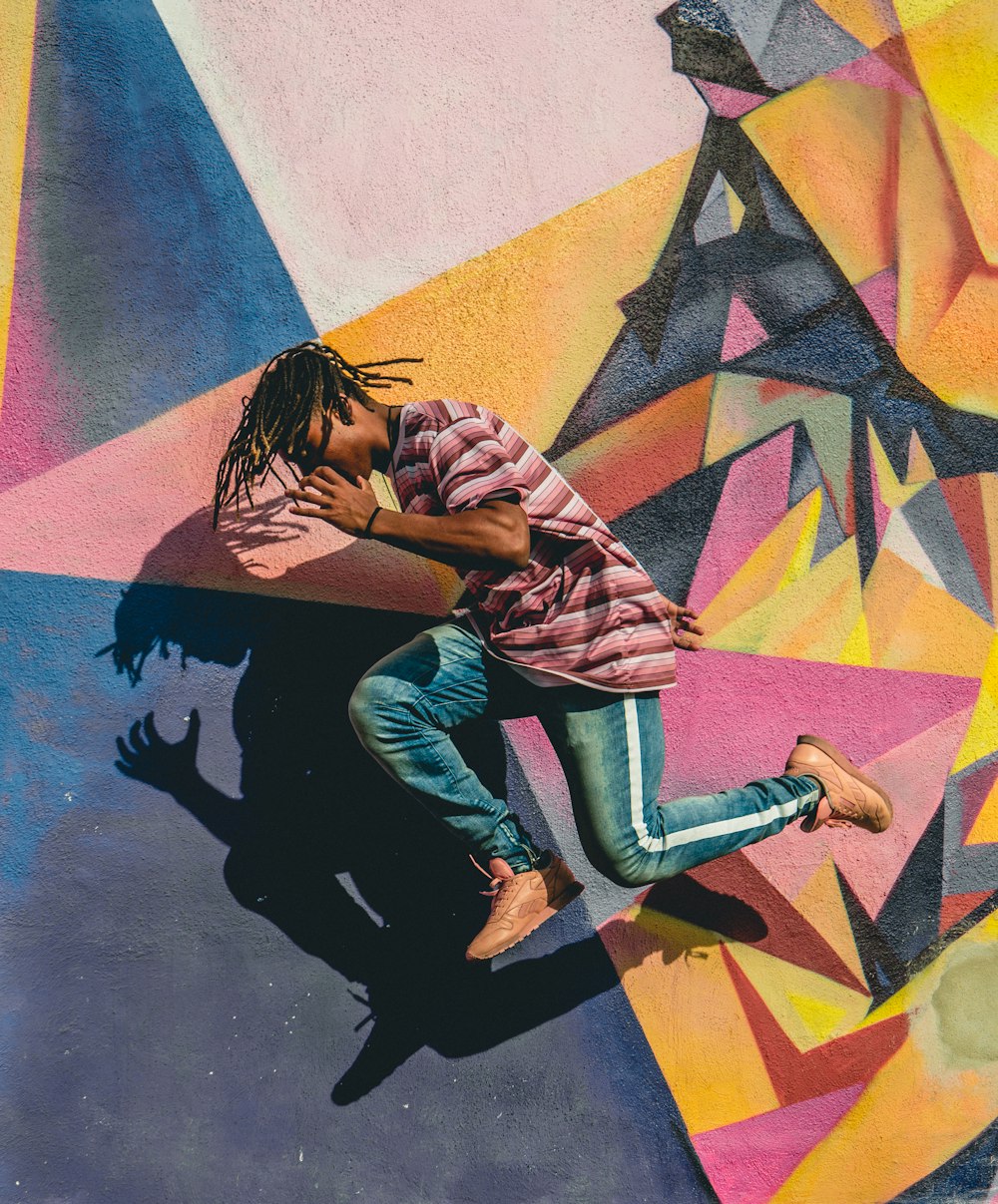 man jumping beside multicolored wall