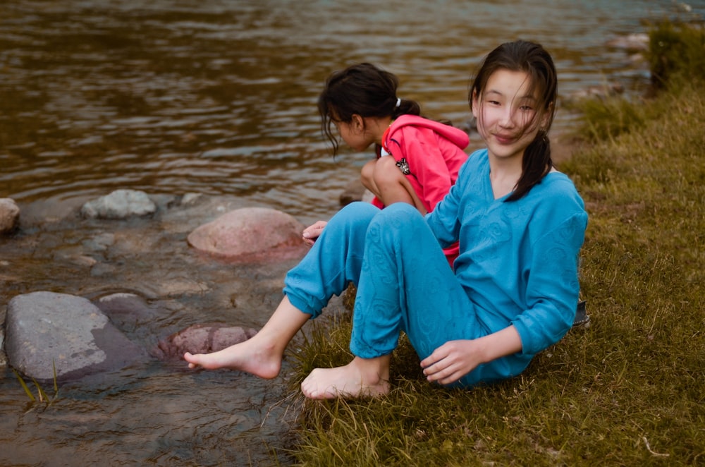 woman in blue V-neck long-sleeved shirt and pants beside girl in pink hooded jacket sitting by the river during daytime