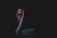 A person is partially obscured by shadows, with one side of their face visible and the other hidden. Their hand is pressed against their face, creating a mysterious and introspective appearance. The lighting is low, emphasizing the contrast between light and shadow.