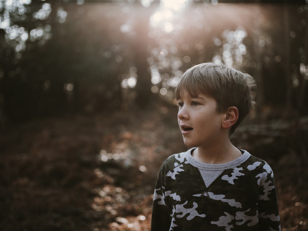 a young boy is standing in the woods