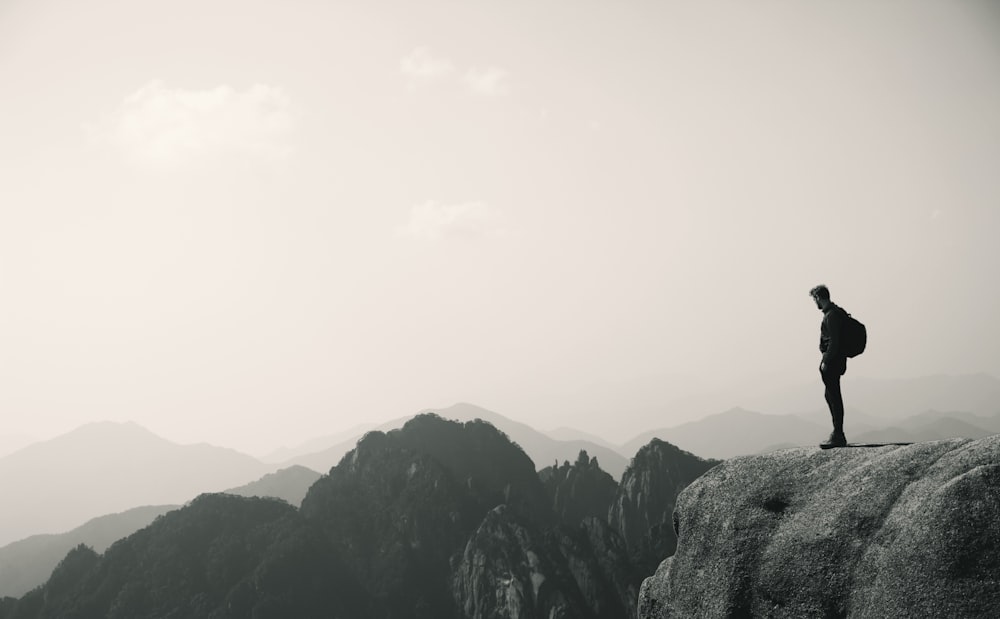 gray scale photography of person standing on rock formation