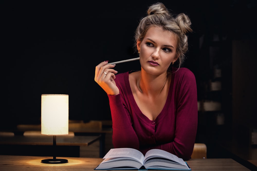 Femme assise à côté d’un livre ouvert tenant un crayon