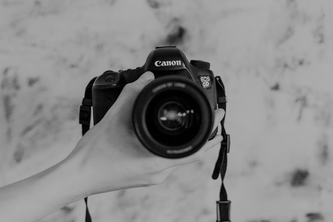 grayscale photography of person holding Canon DSLR camera