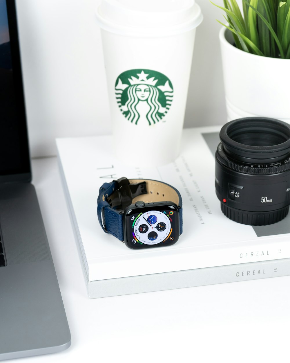 Starbucks coffee, black smart watch and black camera lens on white book