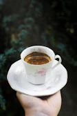 Barista pouring freshly brewed coffee into a delicate cup with purple and gold decor in the background
