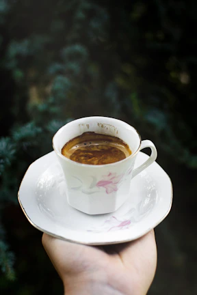 Barista pouring freshly brewed coffee into a delicate cup with purple and gold decor in the background