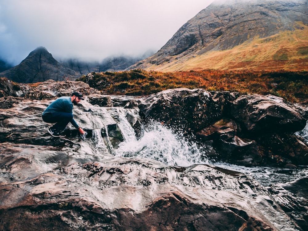 man wearing black shirt sitting near flowing water during daytime