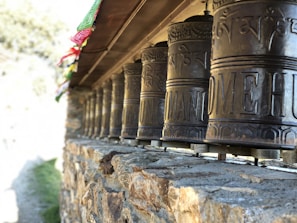 A close-up of a Bhutanese prayer wheel spinning gently beside colorful prayer flags fluttering in the breeze.