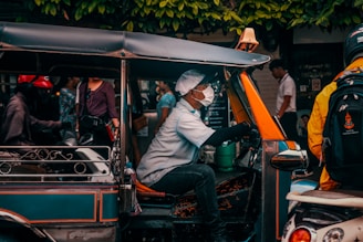 A smiling Bong Tuk Tuk driver standing next to his remorque, with Phnom Penh’s cityscape softly blurred in the background.