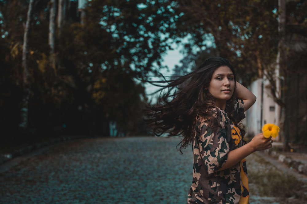 Mujer sosteniendo una flor de pétalos amarillos en el camino