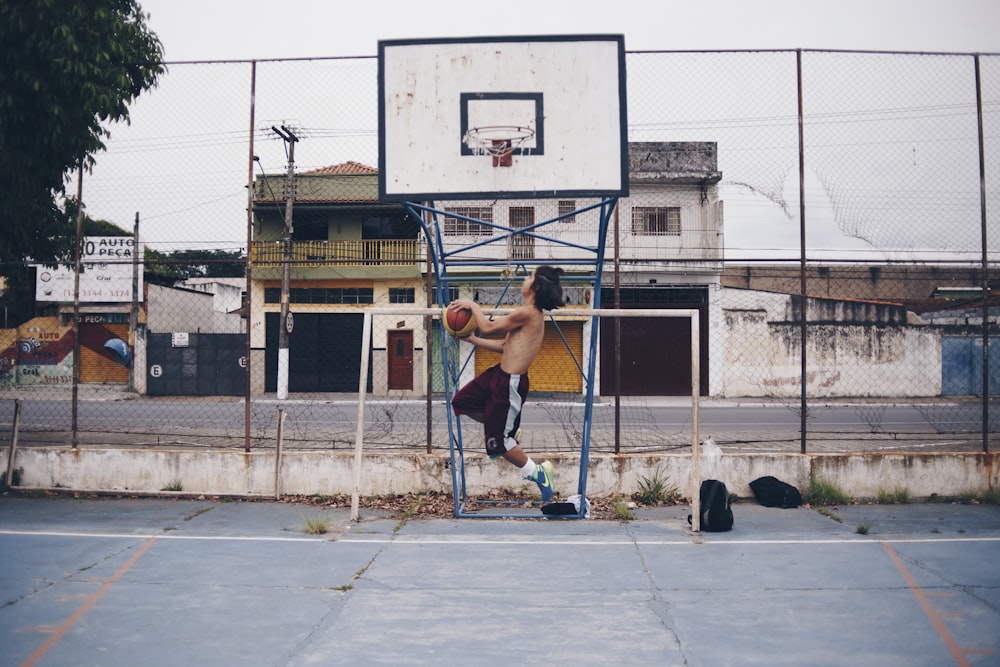man wearing brown shorts doing lay-up near basketball ring during daytime