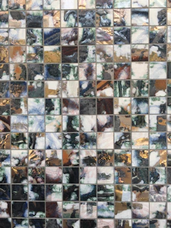 Mosaic art piece featuring shimmering glass tiles in gold and cream hues, reflecting light beautifully.