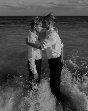 grayscale photo of two man standing on body of water