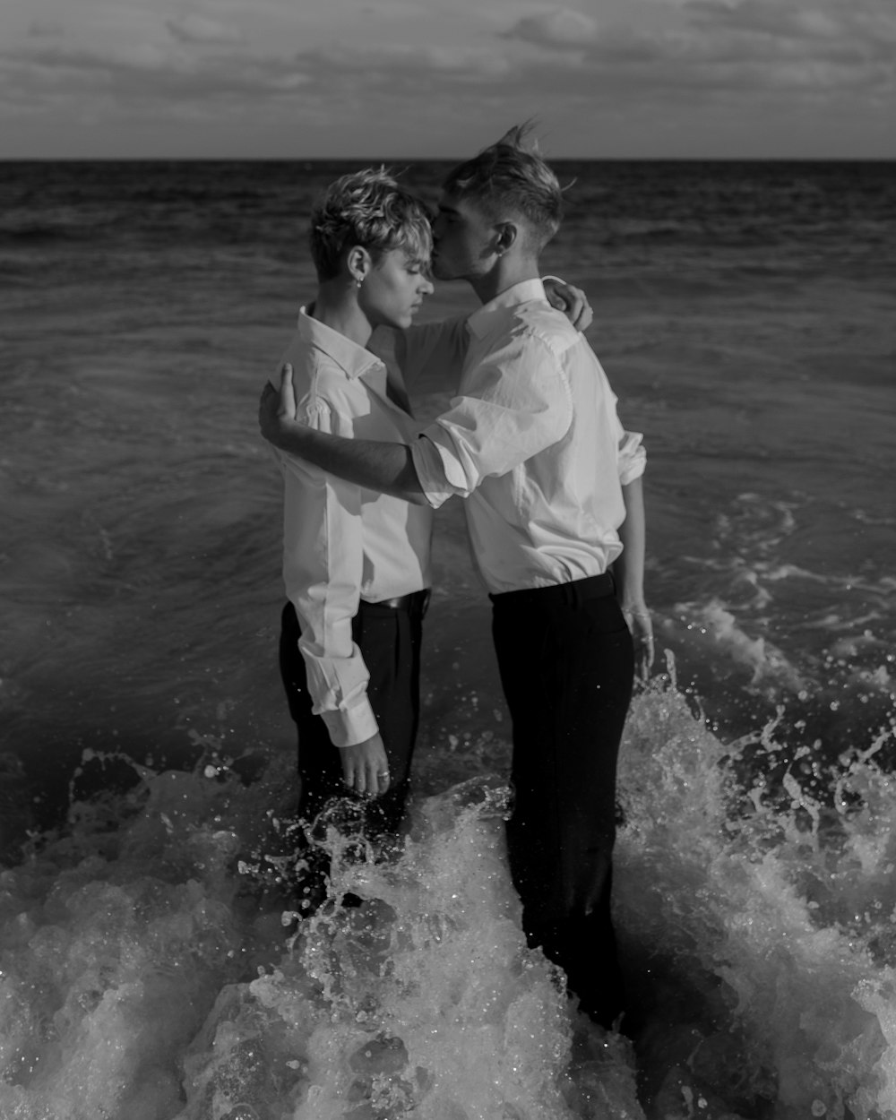 grayscale photo of two man standing on body of water