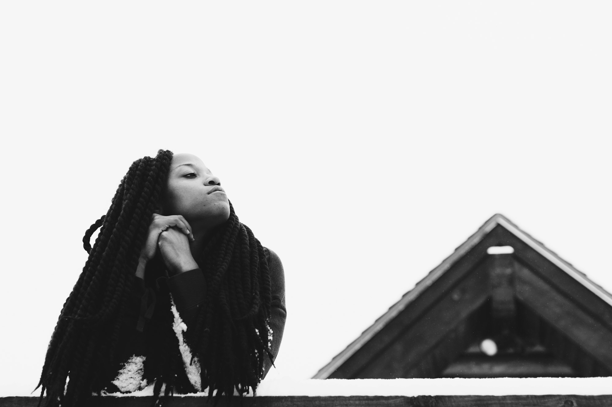 Young woman rests her elbows on a snow-covered railing and gazes upwards into the sky.